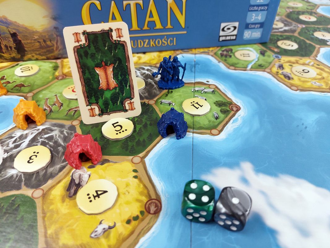 elementy gry Catan: Świt ludzkości, kostki do gry, karta skóry, figurki osadników